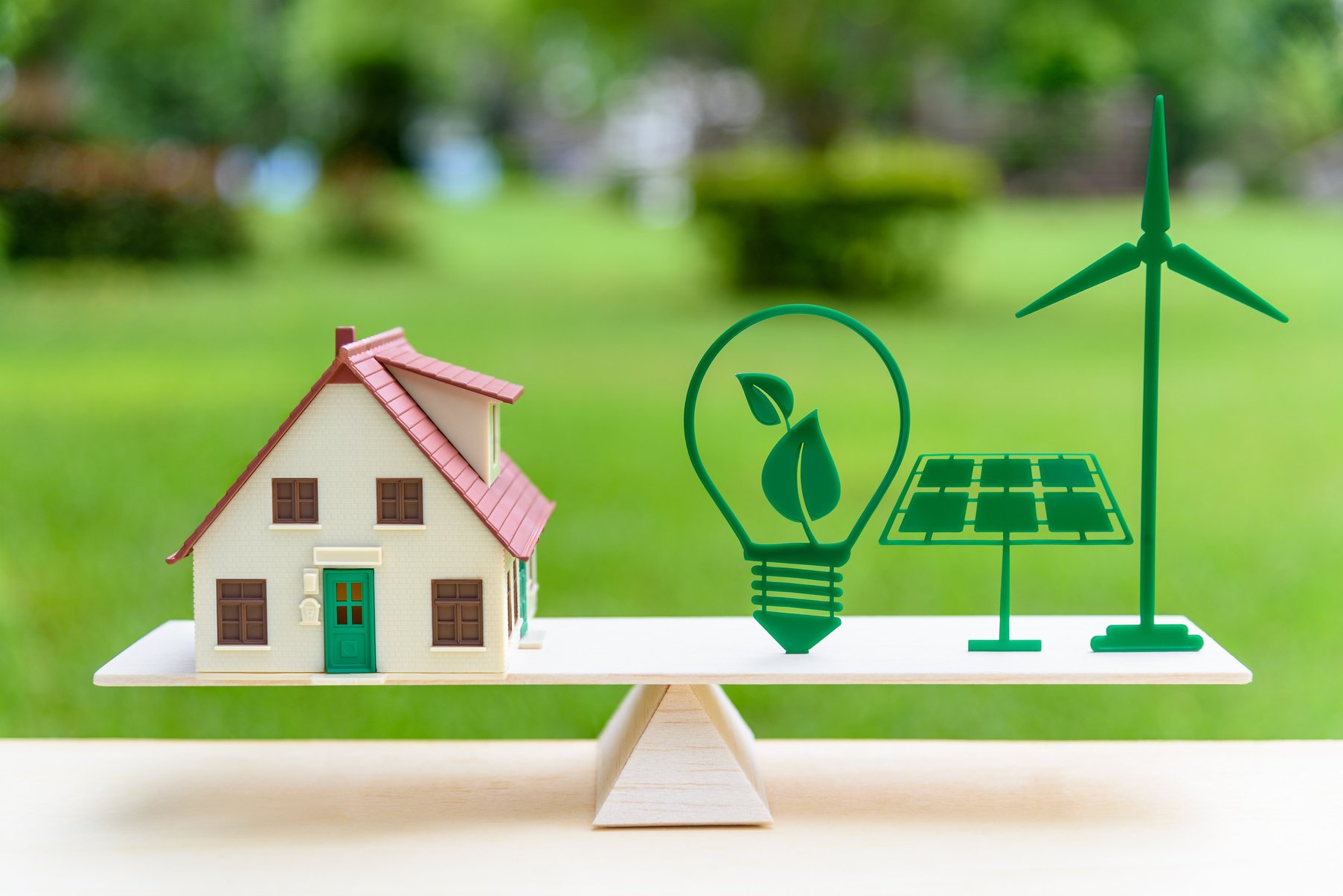 Future clean / renewable or alternative energy for modern living concept : House model, light bulb with green leaf, solar panel, wind mill on wood balance scale, depicts the awareness of environment.